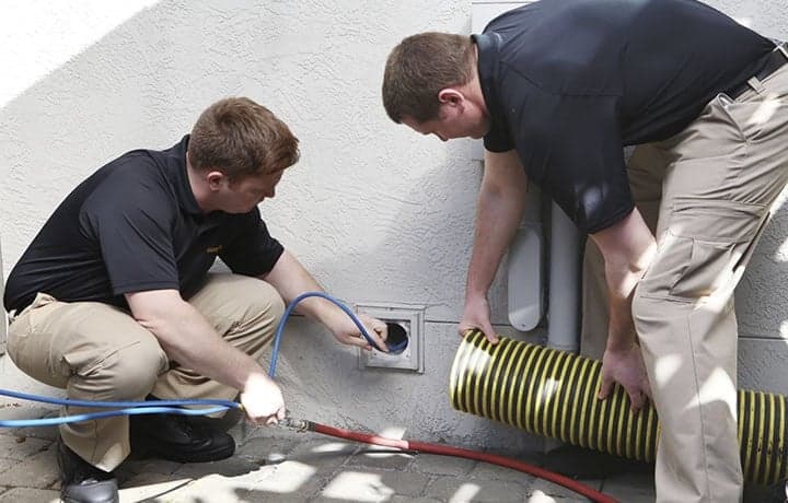 Stanley Steemer technicians inspecting a dryer vent opening on the exterior of a home.
