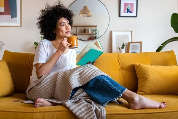 Woman on Couch woman relaxing on couch in clean home enjoying a drink and reading a book