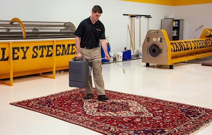 Oriental-Rug-Cleaning-Certified-Technician-Cleaning-Rug Stanley Steemer technician spraying rug protector on an oriental area rug.