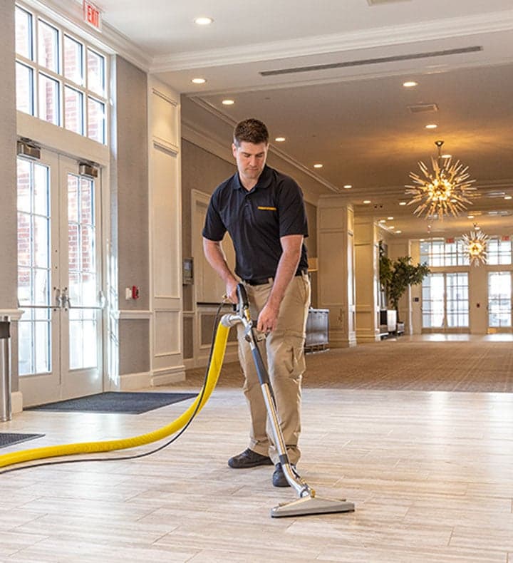 A Stanley Steemer Technician Pulls a Cleaning Wand Across Vinyl Tile Flooring in a Hotel Lobby A Stanley Steemer technician pulls a cleaning wand across vinyl tile flooring in a hotel lobby
