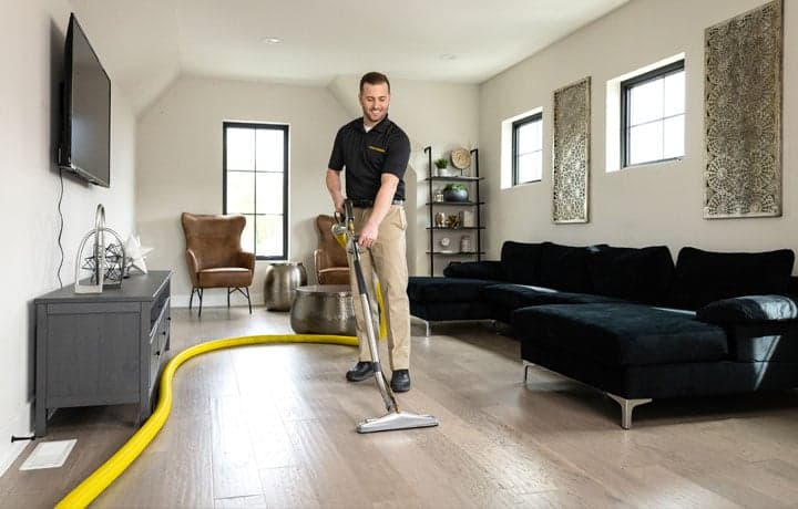 A Smiling Stanley Steemer Technician Pulls a Cleaning Wand Across Vinyl Plank Flooring in a Modern Apartment A smiling Stanley Steemer technician pulls a cleaning wand across vinyl plank flooring in a modern apartment