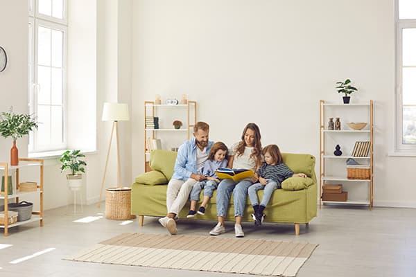 Family Sitting on Couch_Air Duct Maintenance Blog family of four sitting on light green couch reading