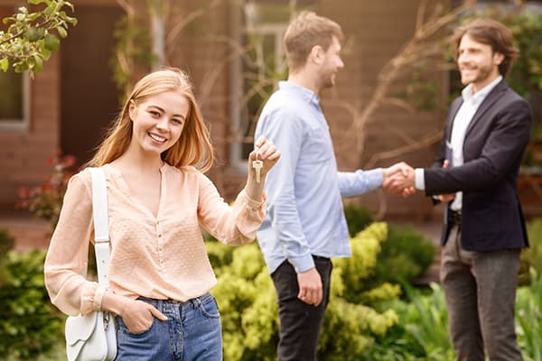 Woman Outside the House woman holding key outside new home man shaking hands with realtor behind her