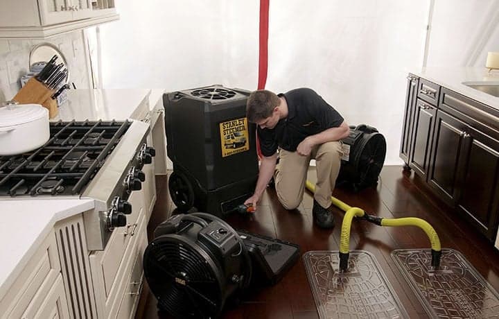 Water-Damage-Restoration-Equipment Stanley Steemer technician setting up water damage restoration equipment in kitchen.